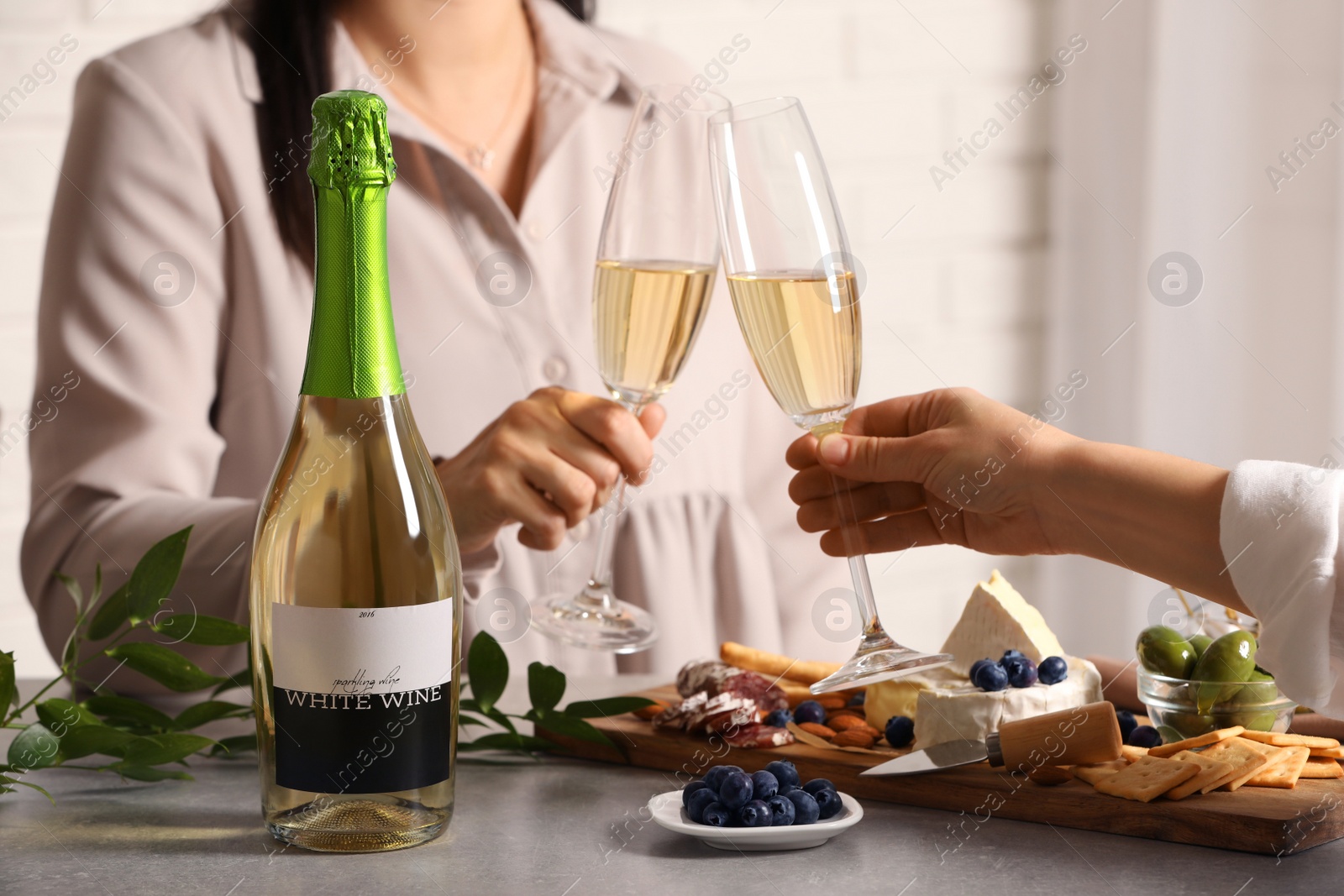 Photo of Women clinking glasses of sparkling wine at table indoors, closeup