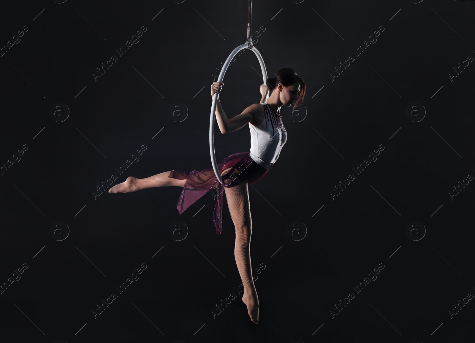 Photo of Young woman performing acrobatic element on aerial ring indoors