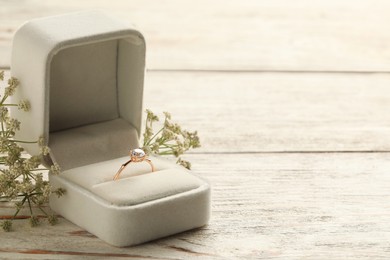 Beautiful engagement ring with gemstone in box and flowers on white wooden table. Space for text
