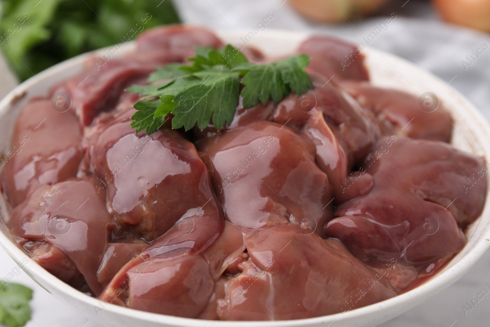 Photo of Bowl of raw chicken liver with parsley on white table, closeup
