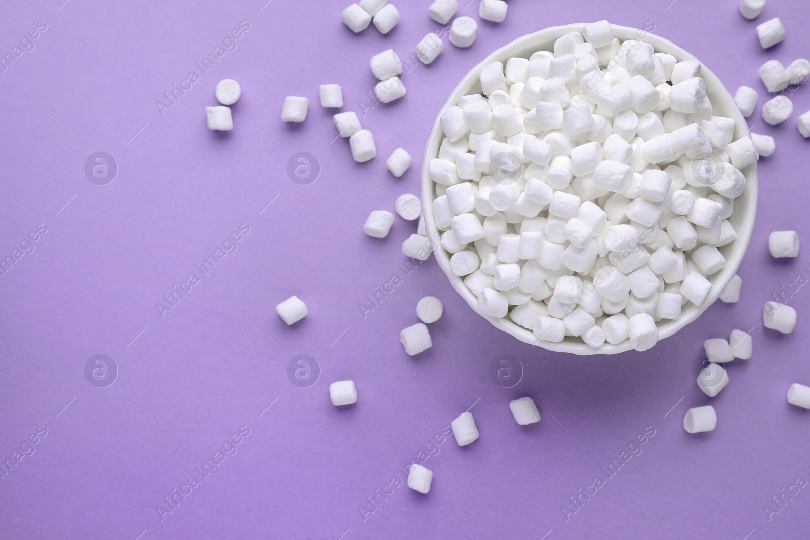 Photo of Bowl with delicious marshmallows on lilac background, flat lay. Space for text