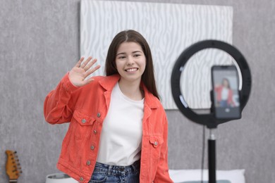 Photo of Smiling teenage blogger waving hello to her subscribers while streaming at home