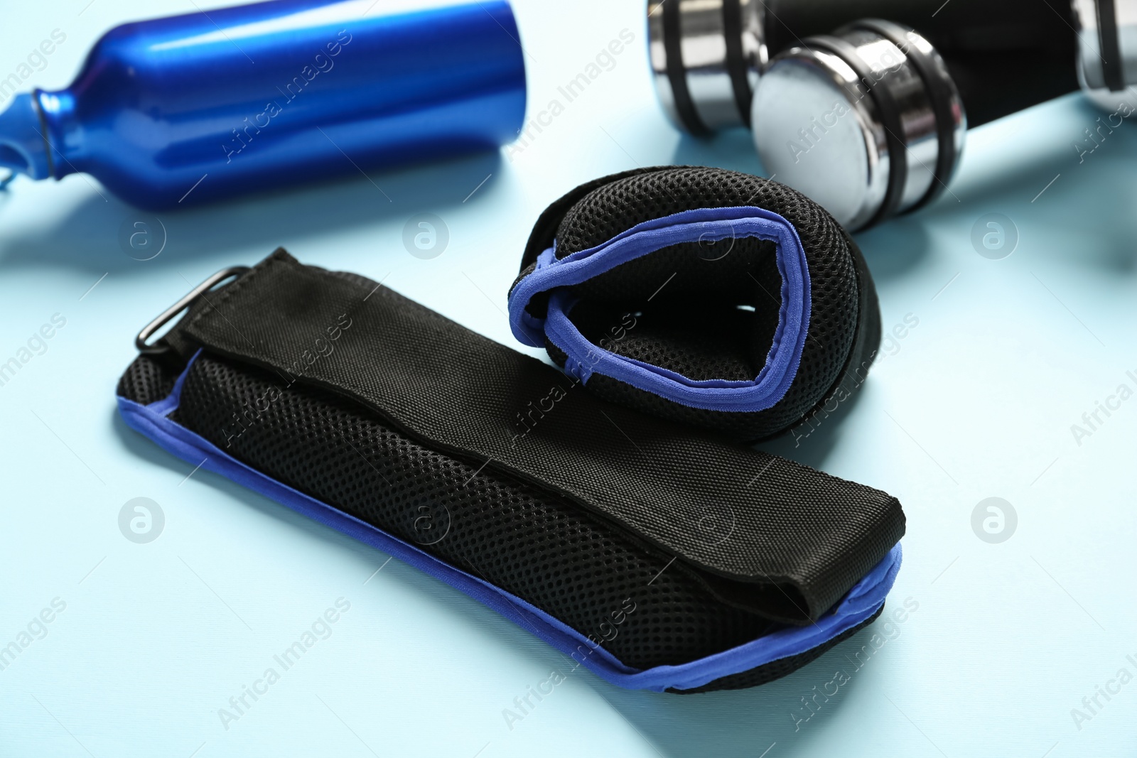 Photo of Weighting agents, dumbbells and sport bottle on light blue background