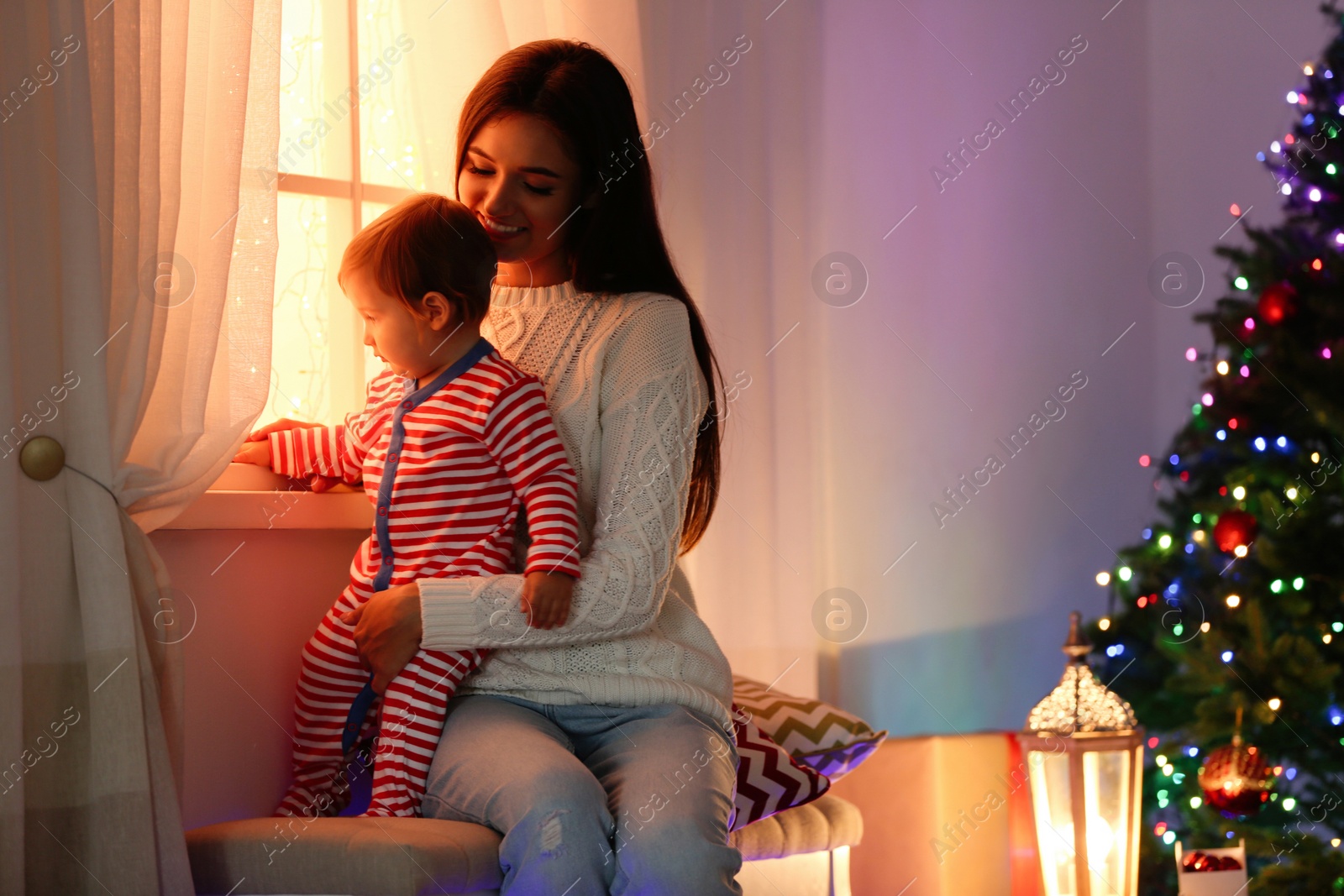 Photo of Mother and her cute baby near window at home. Christmas celebration