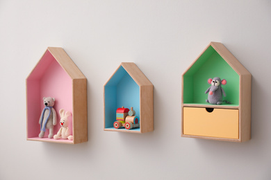 Photo of Stylish house shaped shelves with toys on white wall. Baby room interior design