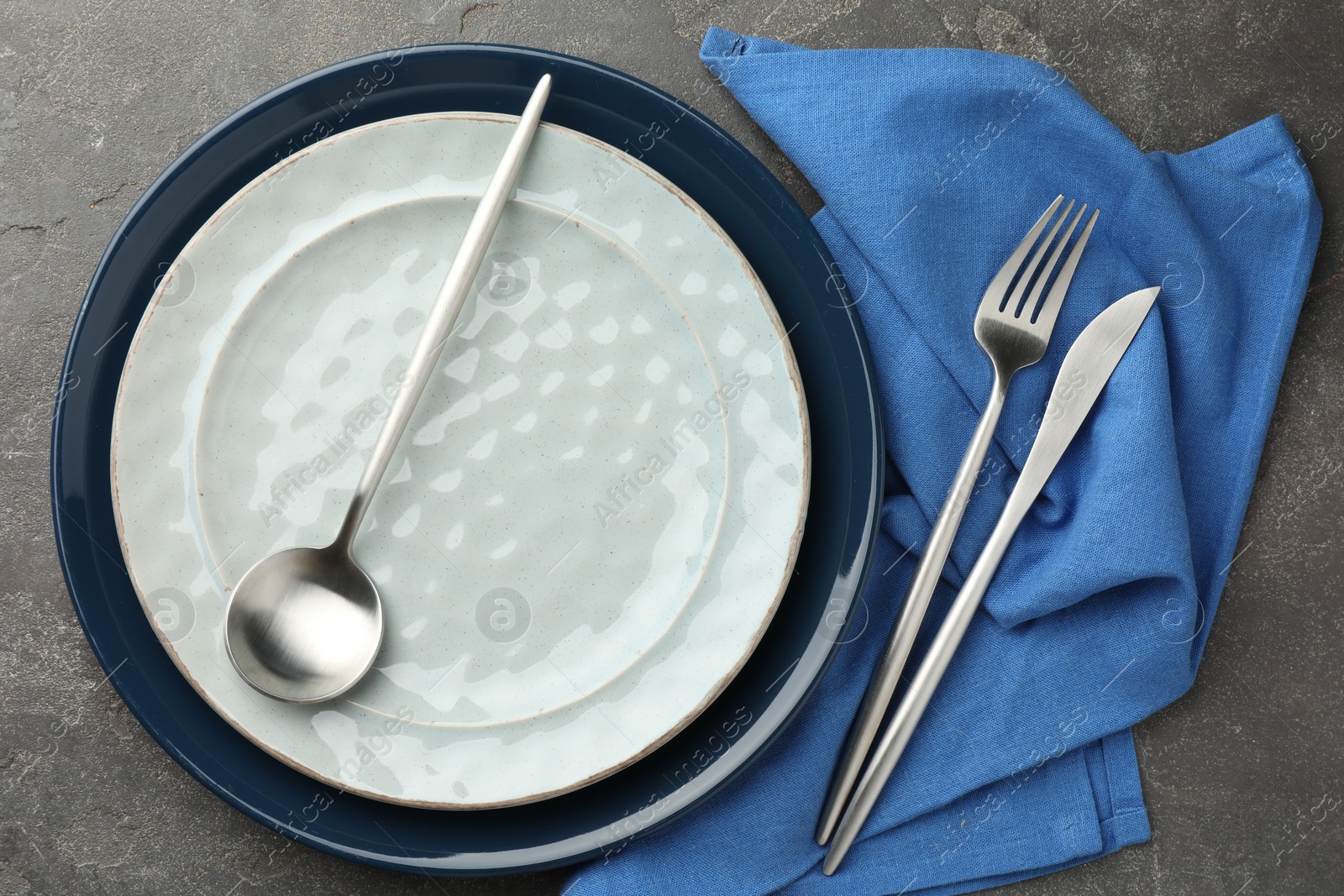 Photo of Stylish setting with cutlery, plates and napkin on grey textured table, flat lay