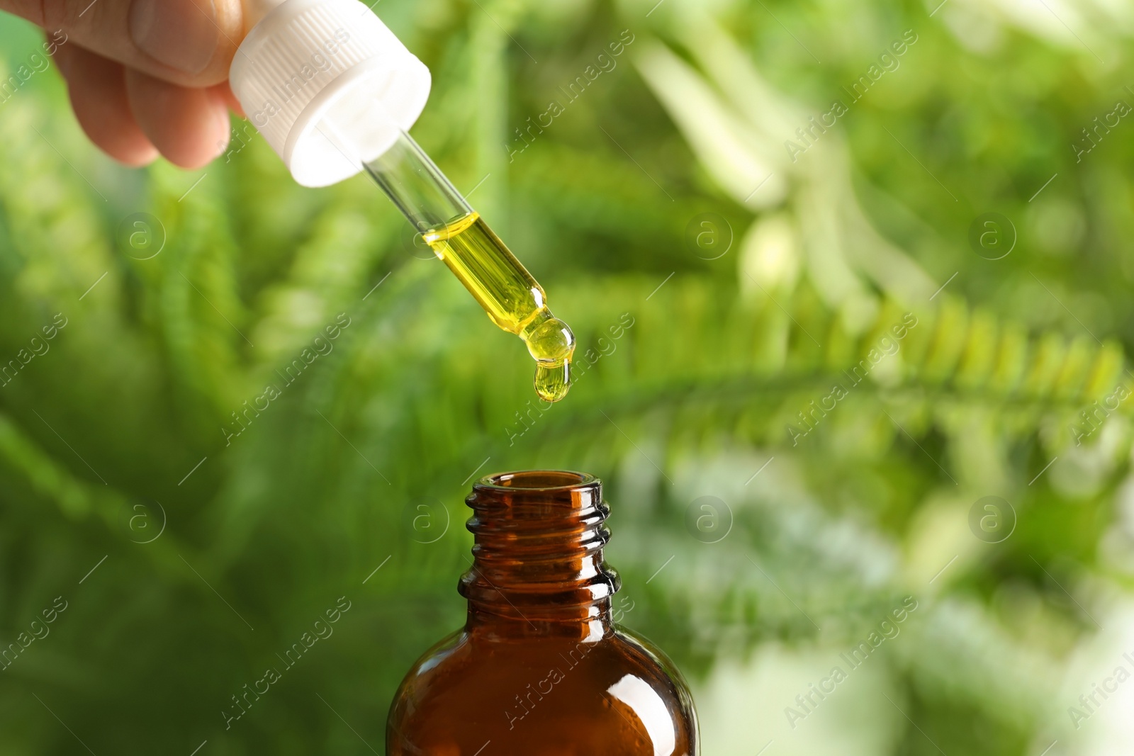 Photo of Woman holding pipette with oil over bottle on blurred background. Space for text
