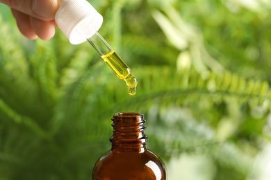 Woman holding pipette with oil over bottle on blurred background. Space for text