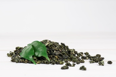 Photo of Heap of dried green tea leaves on white table