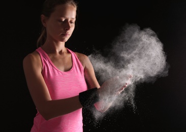 Photo of Young woman applying chalk powder on hands against dark background