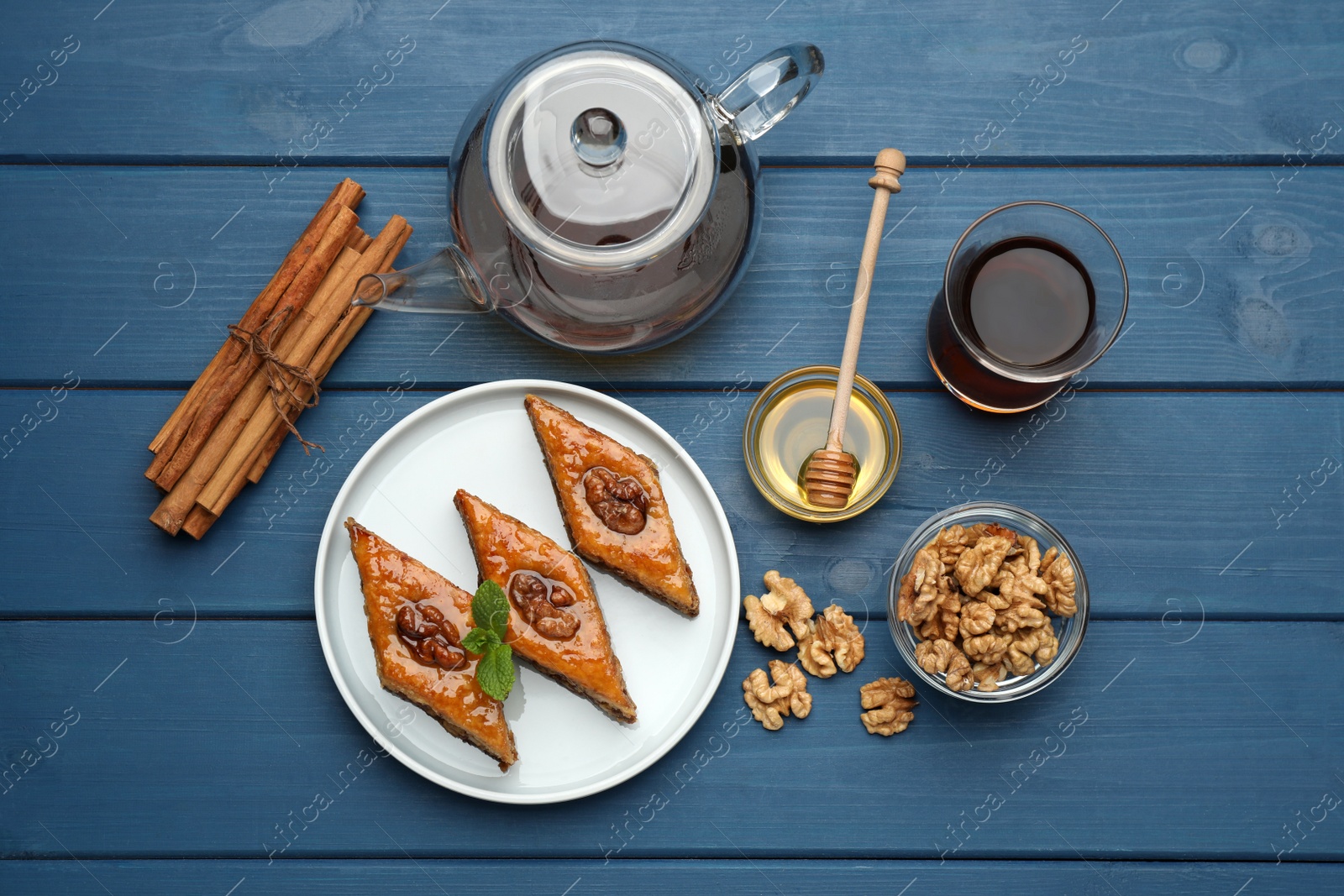 Photo of Delicious sweet baklava with walnuts, honey, cinnamon and hot tea on blue wooden table, flat lay