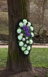Photo of Funeral wreath of flowers on tree outdoors