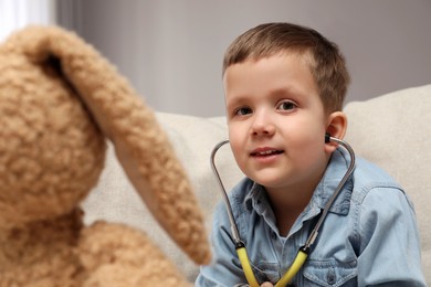 Cute little boy playing with stethoscope and toy bunny indoors. Future pediatrician