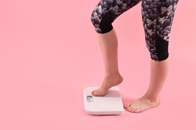 Photo of Woman stepping on floor scale against pink background, closeup. Space for text
