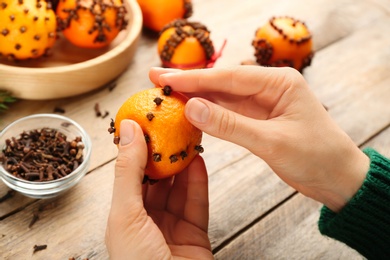 Photo of Woman decorating fresh tangerine with cloves at wooden table, closeup. Making Christmas pomander balls