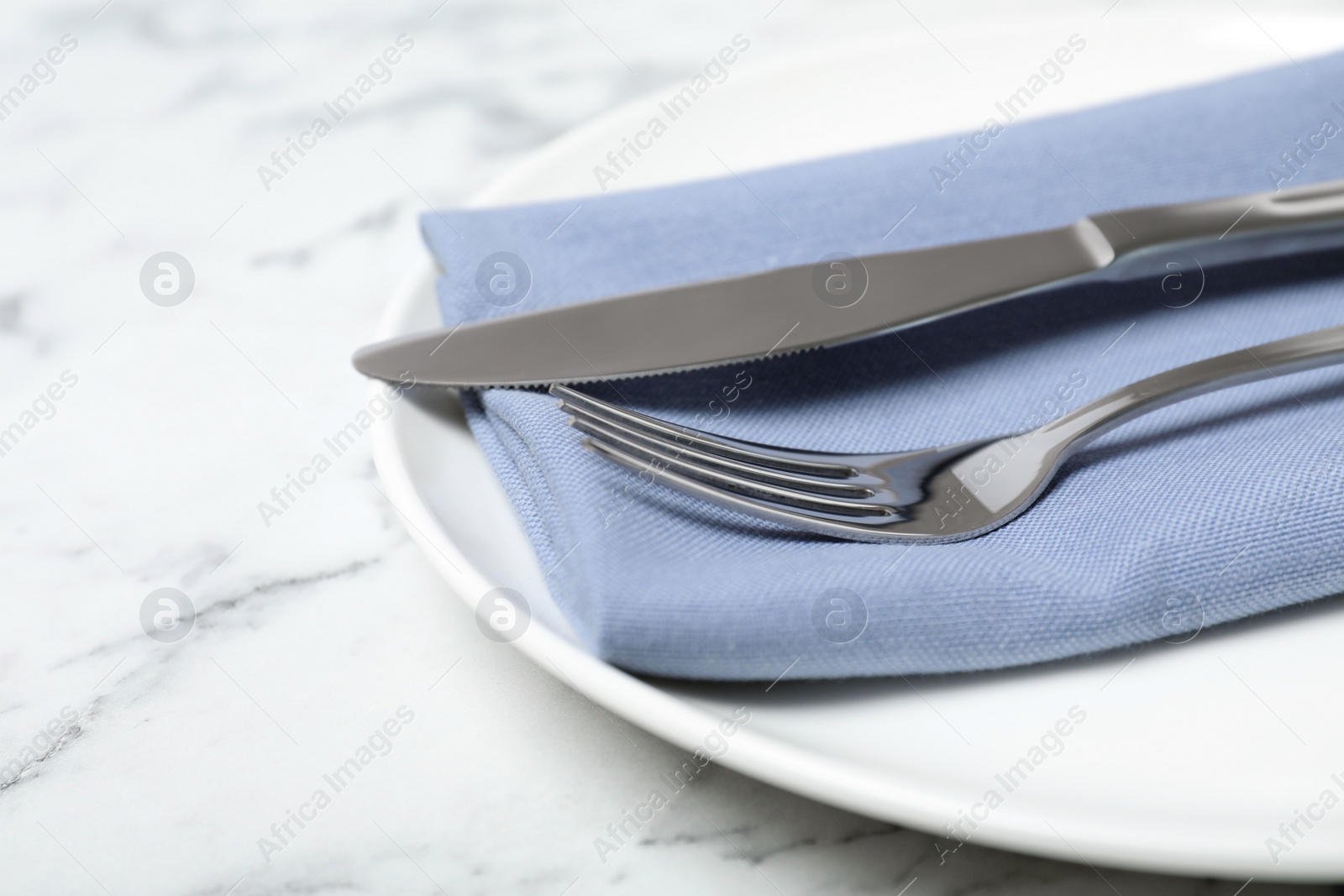 Photo of Plate with cutlery and napkin on marble table, closeup