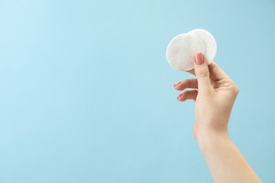 Woman holding cotton pads on light blue background, closeup. Space for text