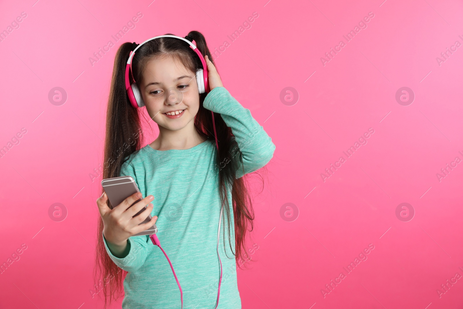 Photo of Cute girl with mobile phone enjoying music in headphones on color background. Space for text