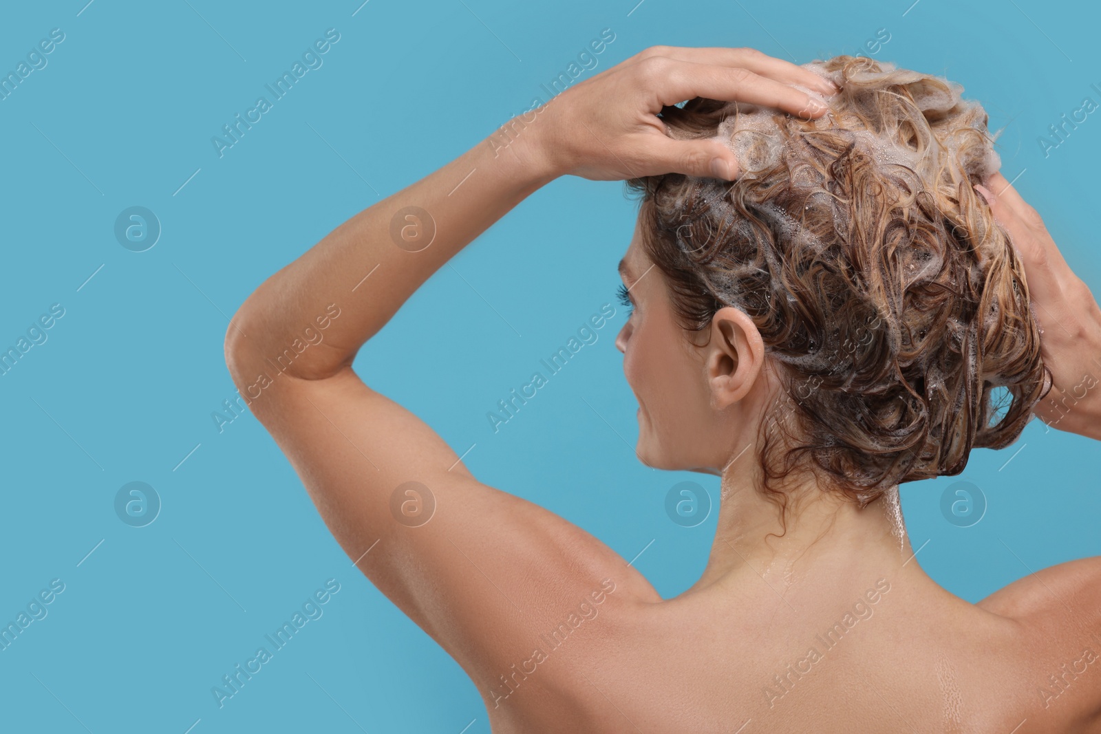 Photo of Woman washing hair on light blue background, back view