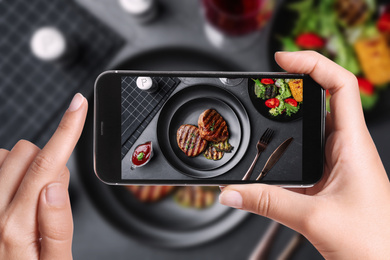 Image of Blogger taking picture of delicious beef medallions at table, closeup. Food photography