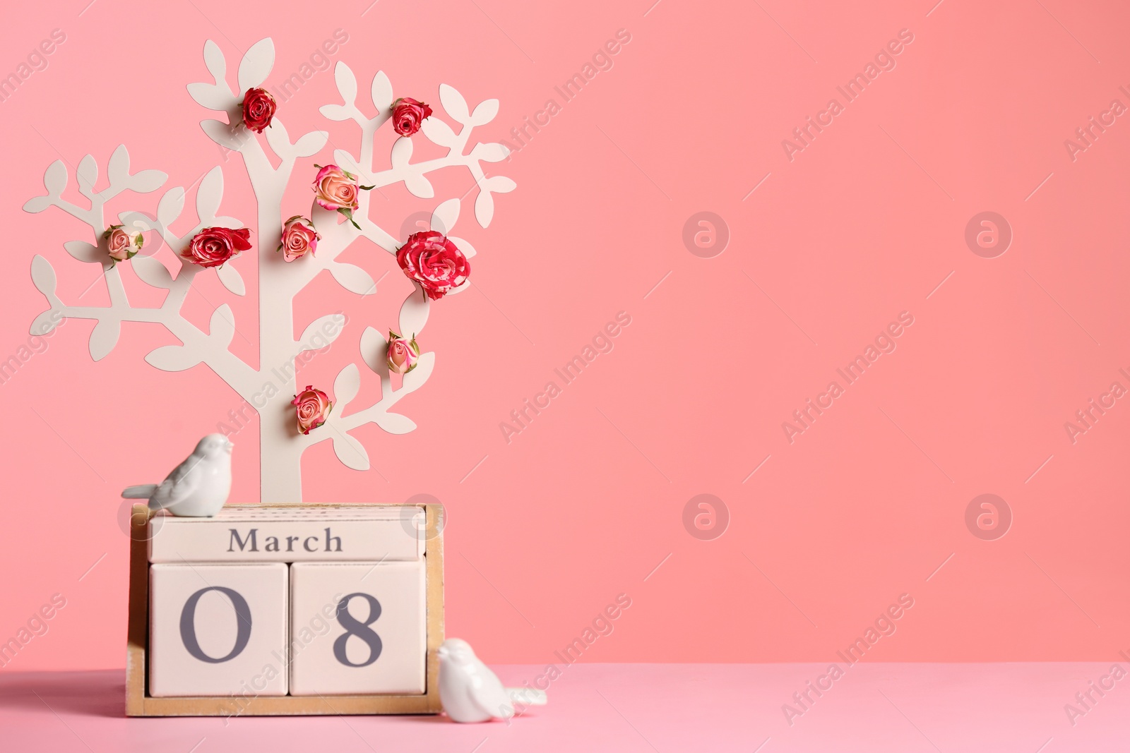 Photo of Decorative tree with flowers and wooden block calendar on table against color background, space for text. Happy Women's Day