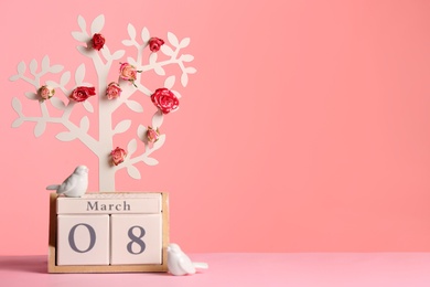 Photo of Decorative tree with flowers and wooden block calendar on table against color background, space for text. Happy Women's Day