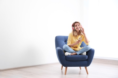 Photo of Young woman listening to music in armchair at home. Space for text