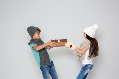 Cute little children in warm clothes with Christmas gift box on light background