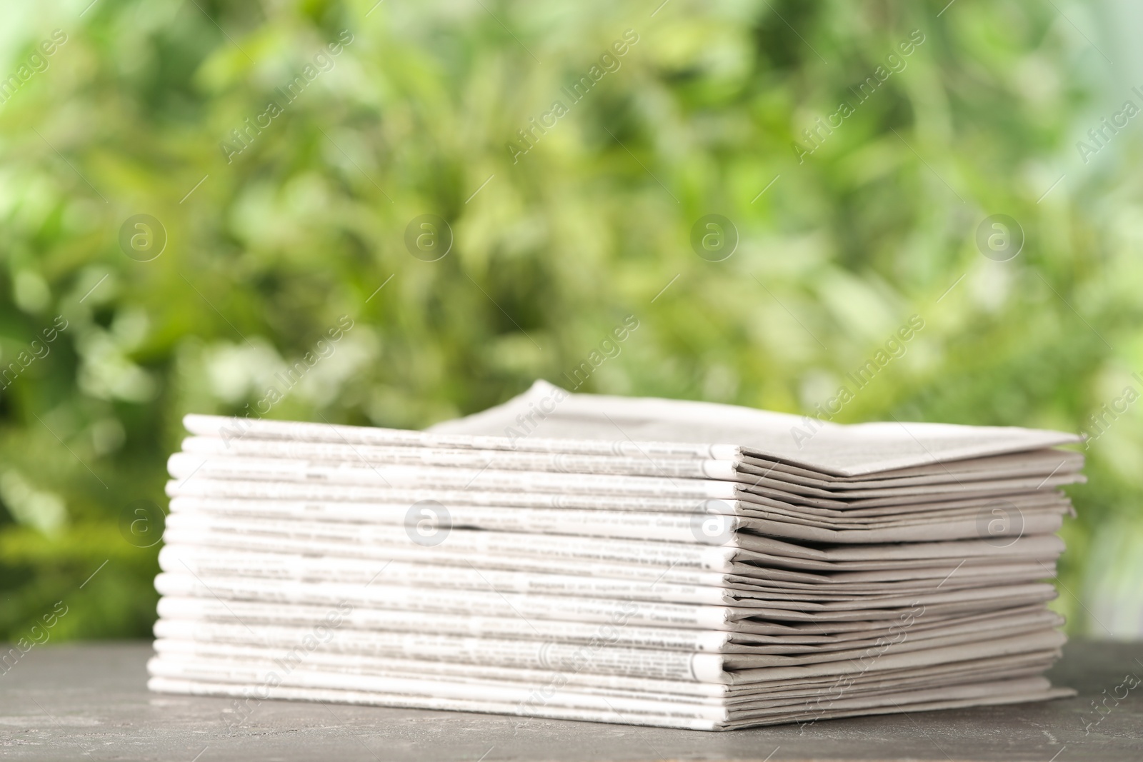 Photo of Stack of newspapers on grey table against blurred green background. Journalist's work