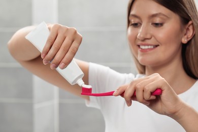 Photo of Young woman applying toothpaste onto brush in bathroom, focus on hands
