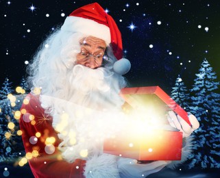 Image of Santa Claus opening gift box in winter forest. Christmas magic