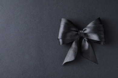 Black ribbon bow on dark background, top view with space for text. Funeral symbol