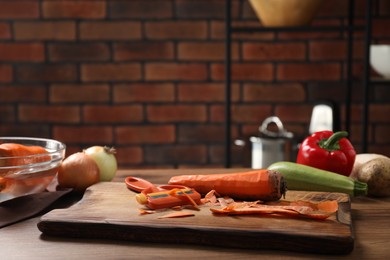 Photo of Peels, peeler and fresh vegetables on wooden table in kitchen