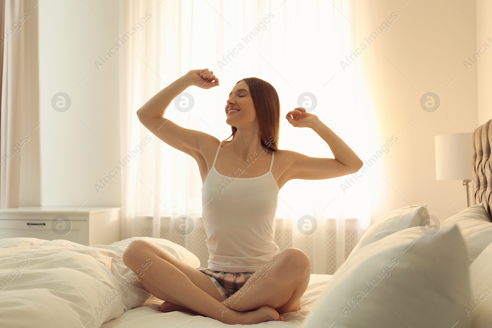 Photo of Young woman stretching on bed at home. Lazy morning