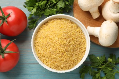 Photo of Raw bulgur in bowl, vegetables and parsley on light blue wooden table, flat lay