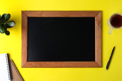 Photo of Clean small chalkboard, coffee, plant and stationery on yellow background, flat lay