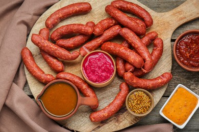 Photo of Delicious sausages, ketchup, mustard and horseradish on wooden table, flat lay
