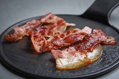 Photo of Slices of tasty fried bacon on grey table, closeup