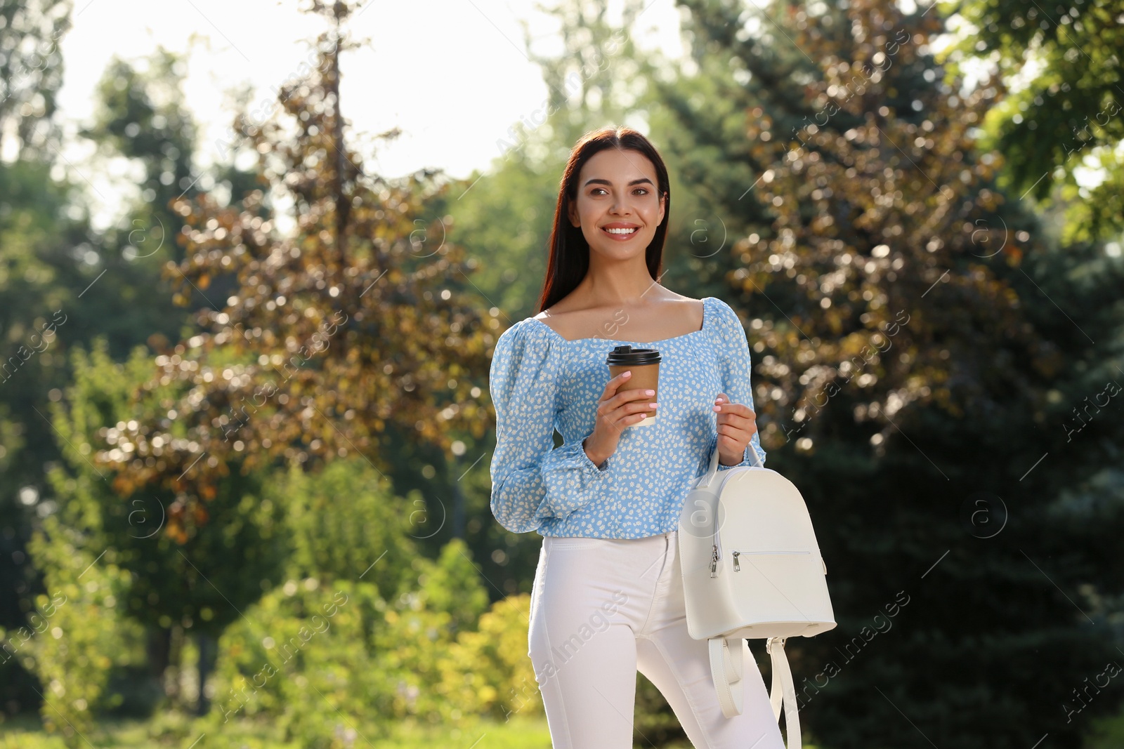 Photo of Beautiful young woman with stylish white backpack and coffee in park, space for text