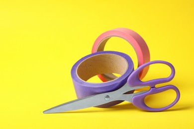 Photo of Two rolls of adhesive tape and scissors on yellow background. Space for text
