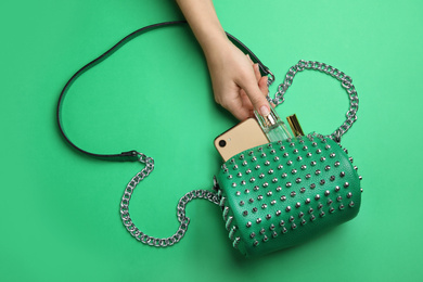 Photo of Woman taking bottle of perfume from small bag on green background, top view