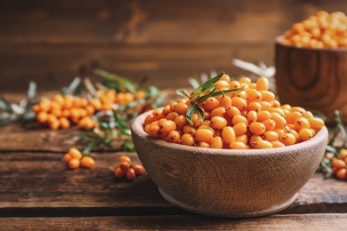 Fresh ripe sea buckthorn in bowl on wooden table. Space for text