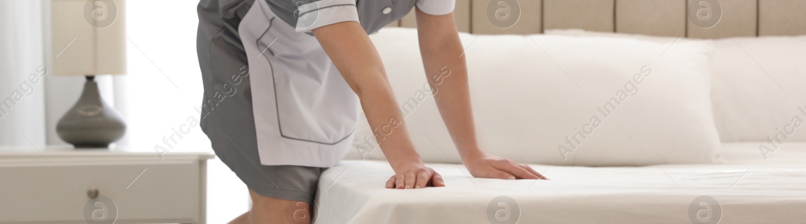 Image of Young chambermaid making bed in hotel room, closeup. Banner design