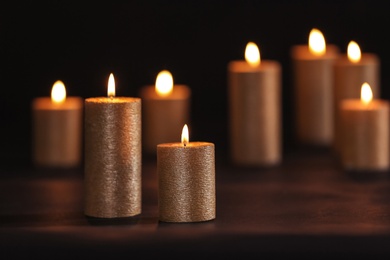 Burning gold candles on table against black background, space for text