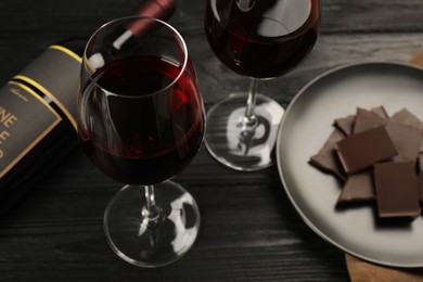 Photo of Tasty red wine and chocolate on black wooden table