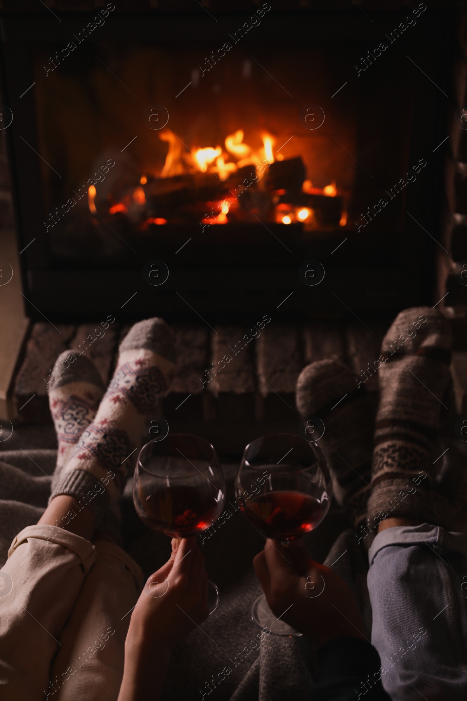 Photo of Couple with glasses of red wine near burning fireplace, closeup