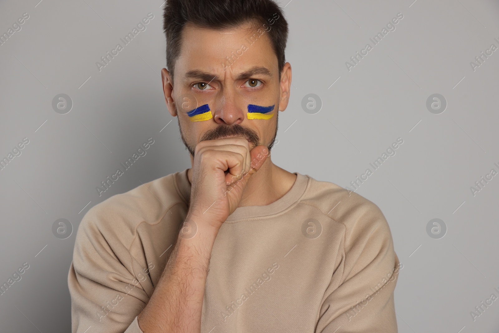 Photo of Angry man with drawings of Ukrainian flag on face against light grey background