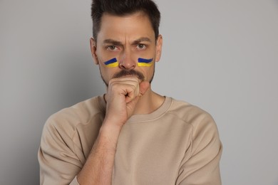 Photo of Angry man with drawingsUkrainian flag on face against light grey background