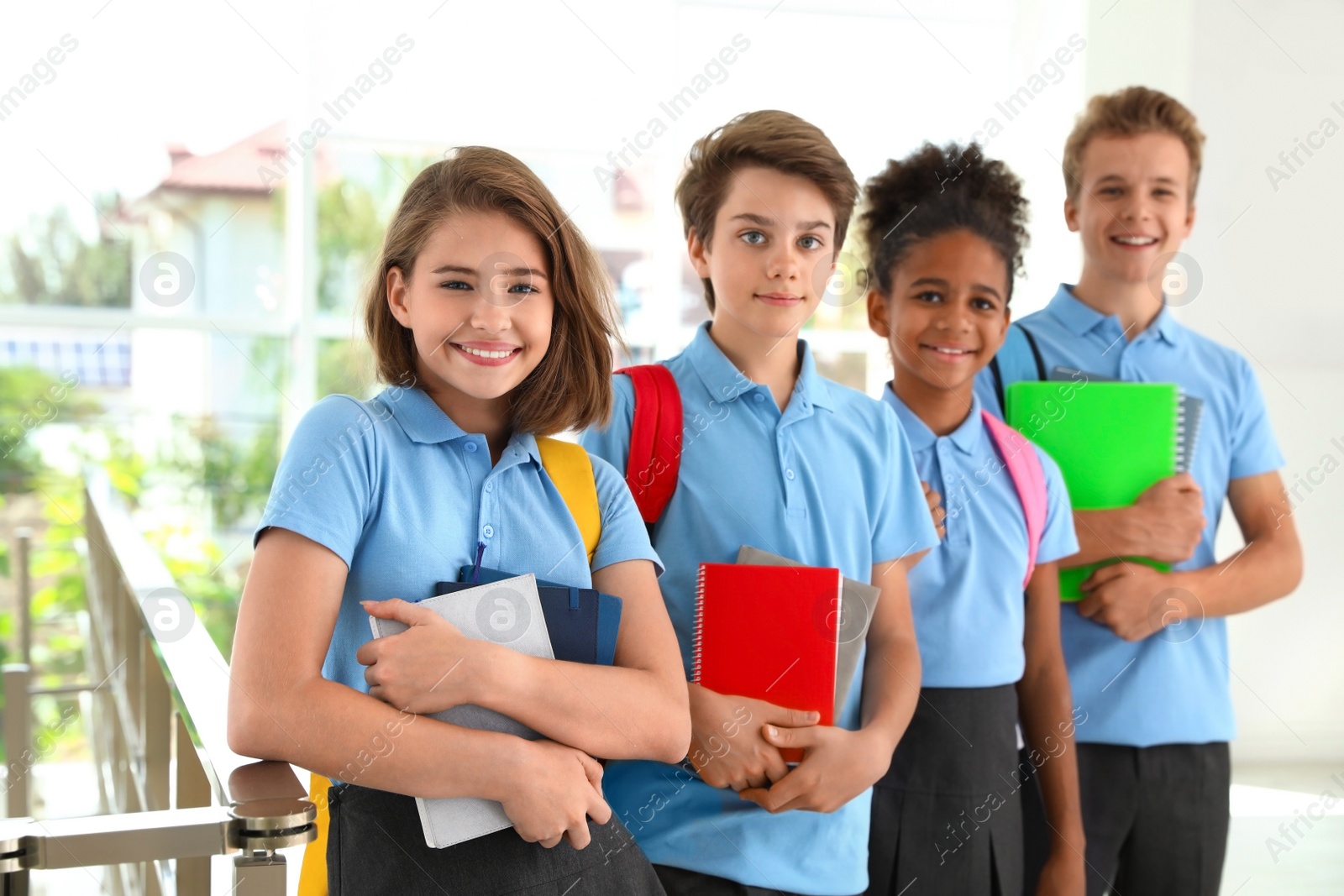 Photo of Happy pupils in school uniform with backpacks indoors