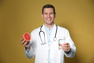 Nutritionist holding glass of pure water and ripe grapefruit on yellow background